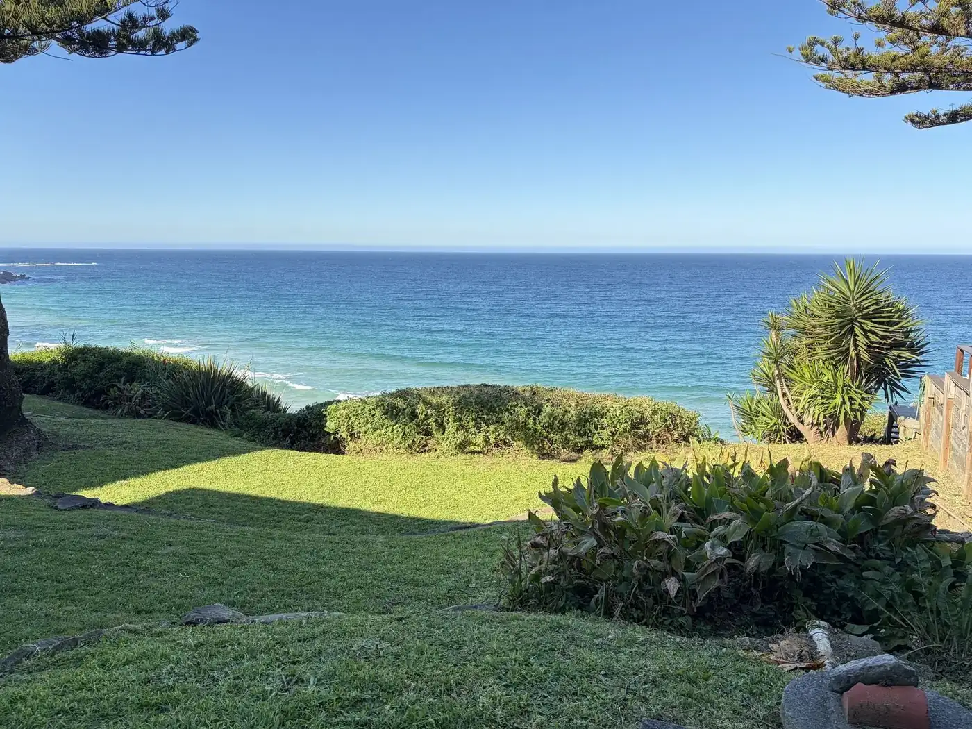 The same clifftop lawn after mowing, short and even, with the hedge trimmed and the ocean behind