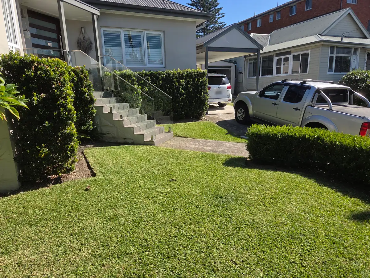 Front lawn freshly mown, with neatly trimmed hedges beside the entry stairs and driveway