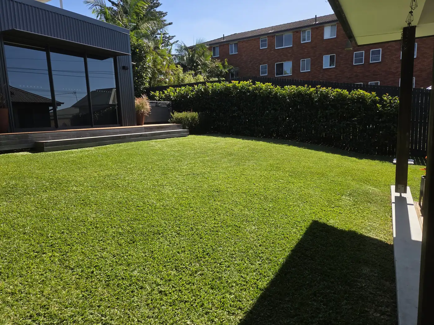 Freshly mown backyard lawn with a neatly trimmed hedge along a dark timber fence